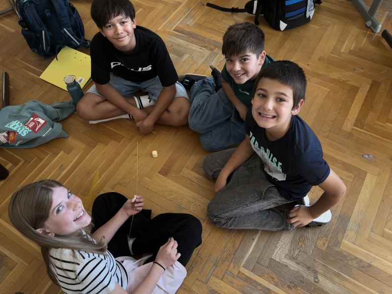 Vier Kinder sitzen auf dem Holzboden und lächeln in die Kamera.